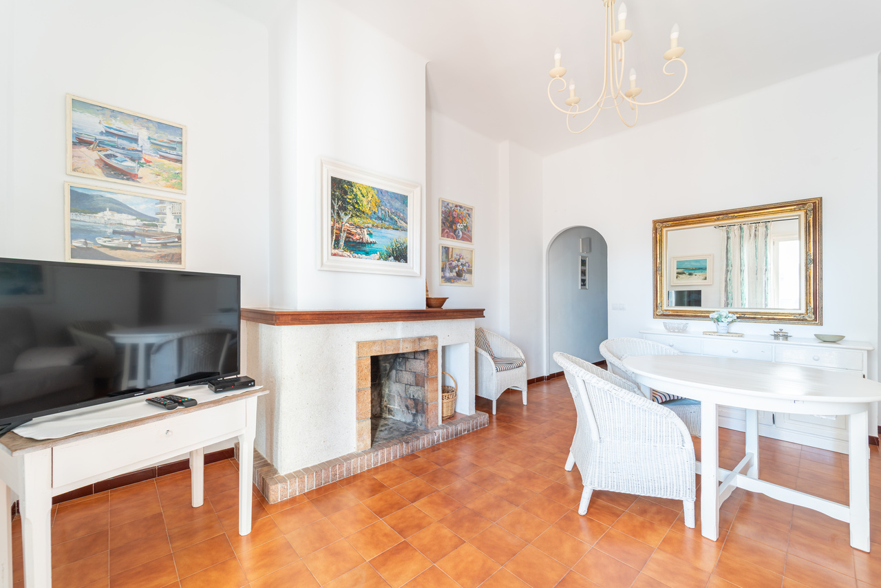 Salón con chimenea de obra, televisión y mesa de comedor con butacas de mimbre.