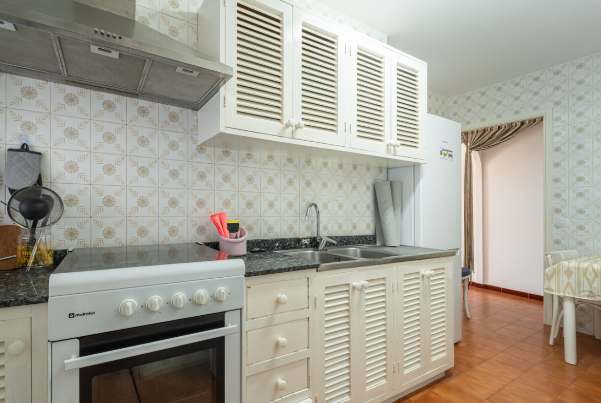 Cocina con cocina de gas y horno, campana extractora y muebles blancos.