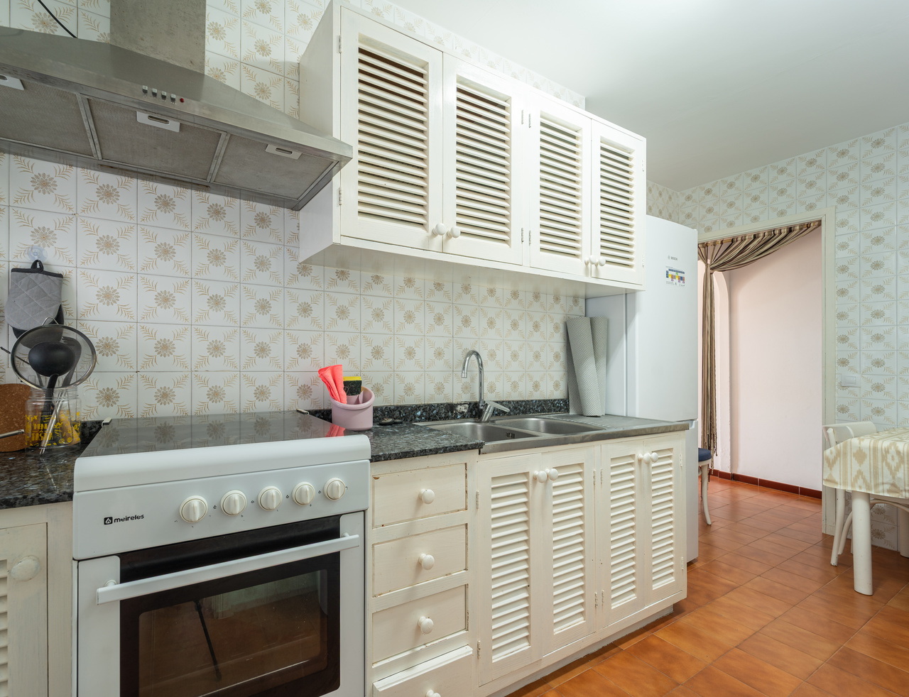 Cocina con cocina de gas y horno, campana extractora y muebles blancos.
