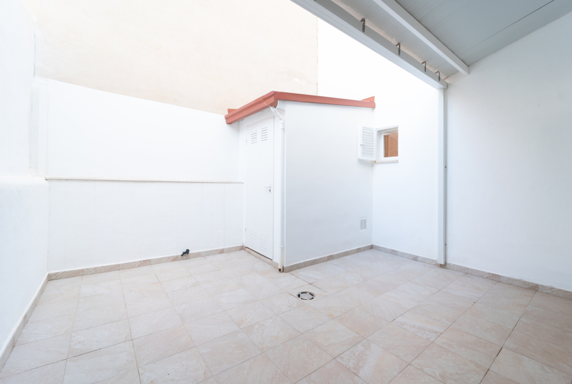 Patio exterior enlosado de la vivienda, de paredes blancas.