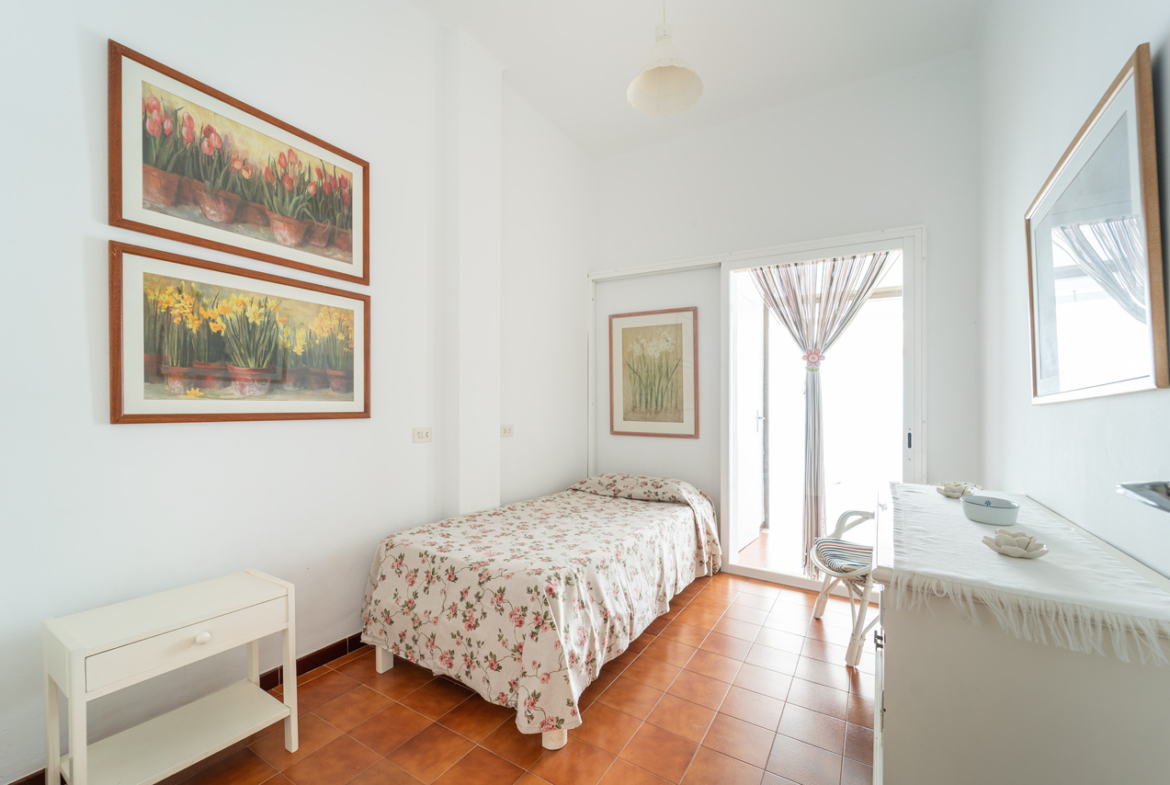Dormitorio con cama, mesita blanca, cómoda y ventana.