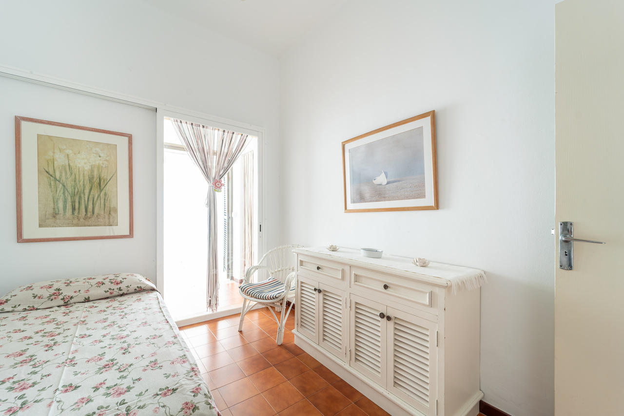 Dormitorio con cama, aparador blanco y salida acristalada.