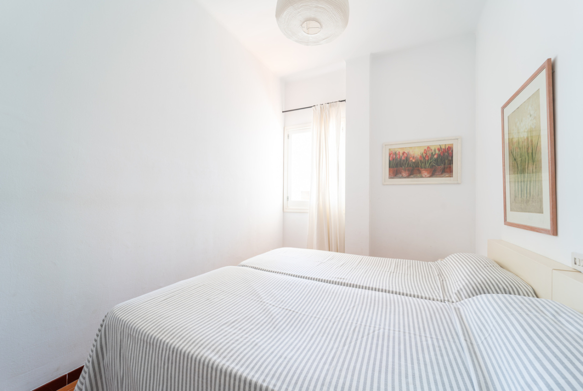 Dormitorio con cama doble, cuadro enmarcado y ventana con visillo.