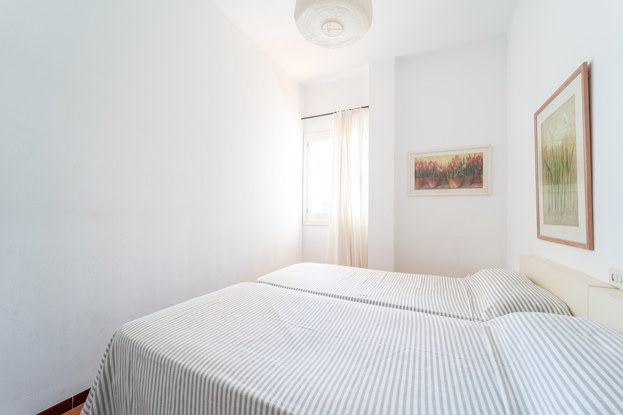 Dormitorio con cama doble, cuadro enmarcado y ventana con visillo.