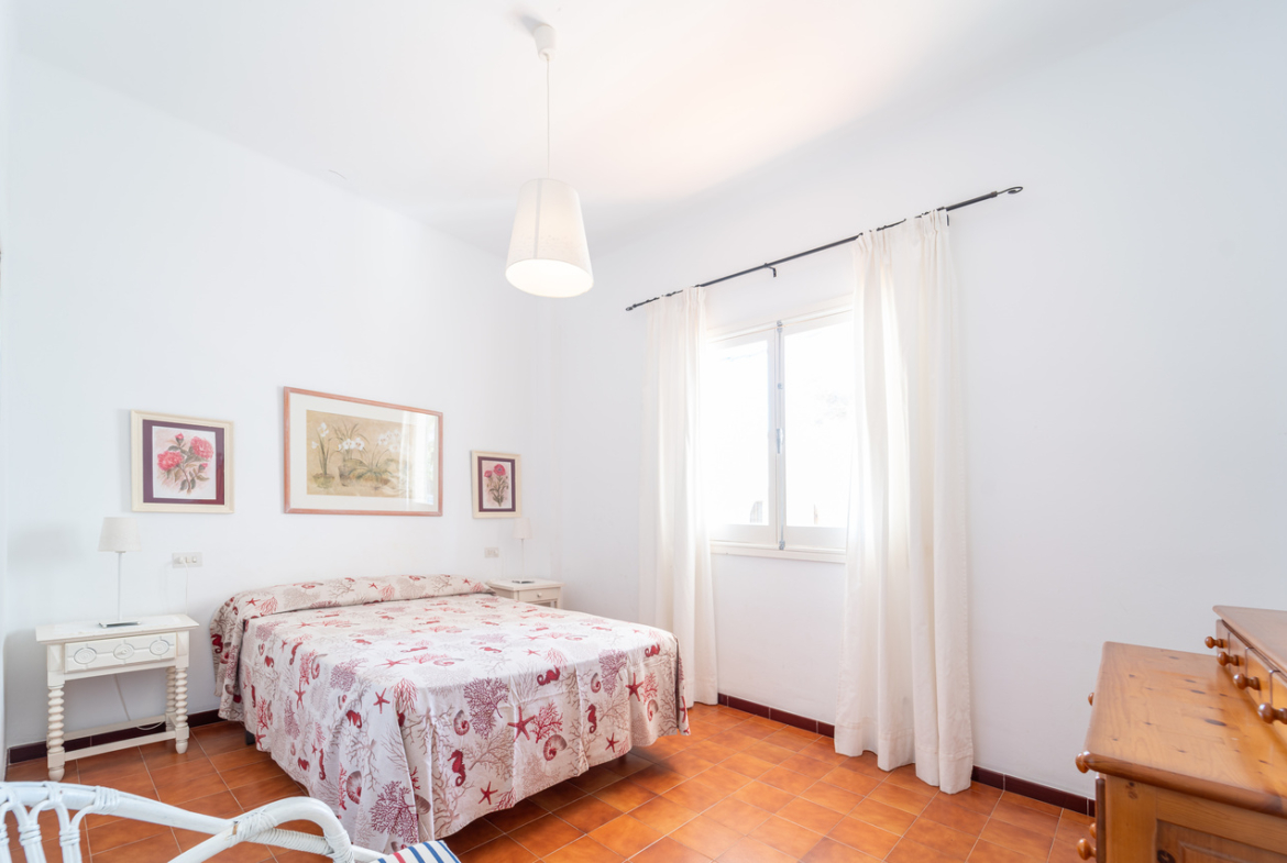 Dormitorio con cama doble, cuadros enmarcados y ventana con cortinas.