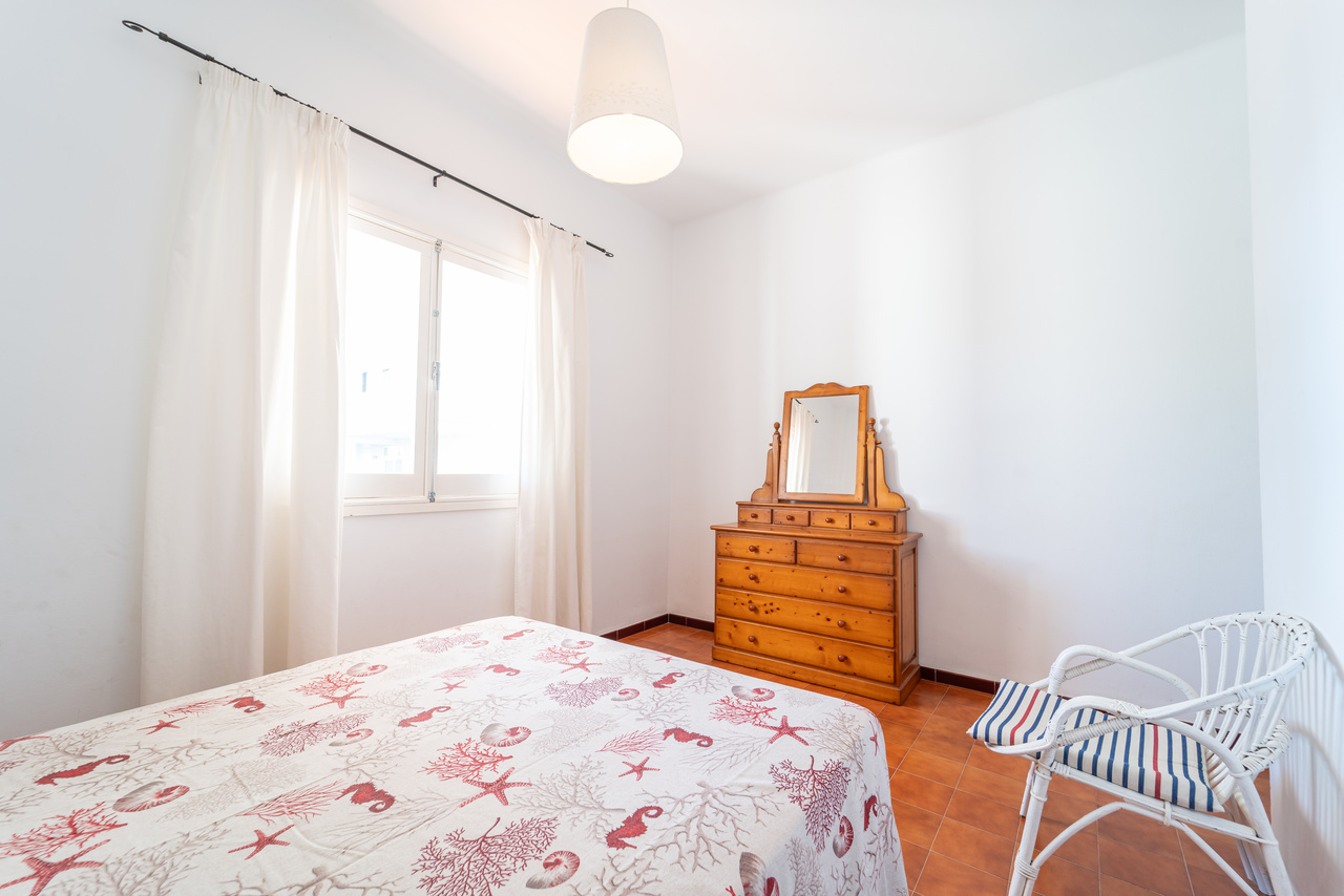 Dormitorio con cama doble, cómoda de madera con espejo y butaca de mimbre.
