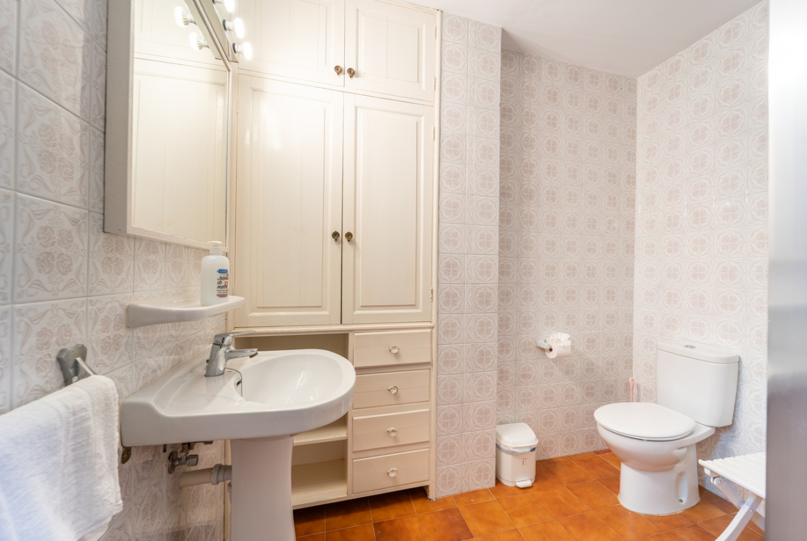 Cuarto de baño con lavabo con pie, inodoro y armario empotrado blanco.