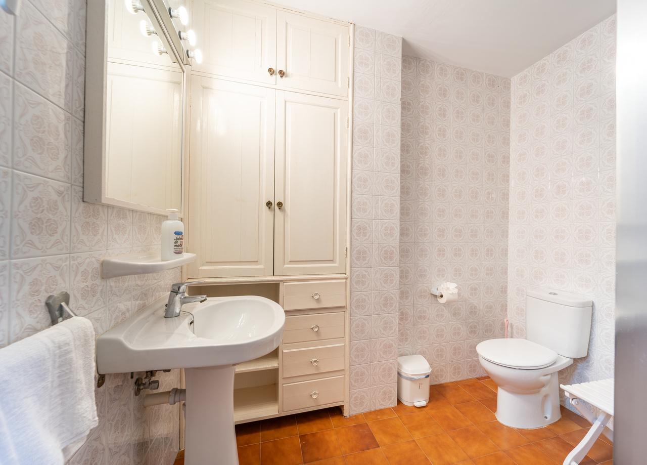 Cuarto de baño con lavabo con pie, inodoro y armario empotrado blanco.