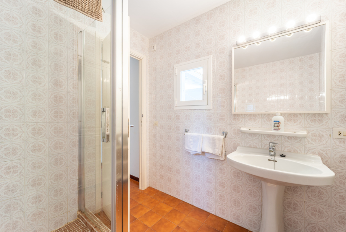 Cuarto de baño con ducha con mampara, lavabo con pie y espejo iluminado.