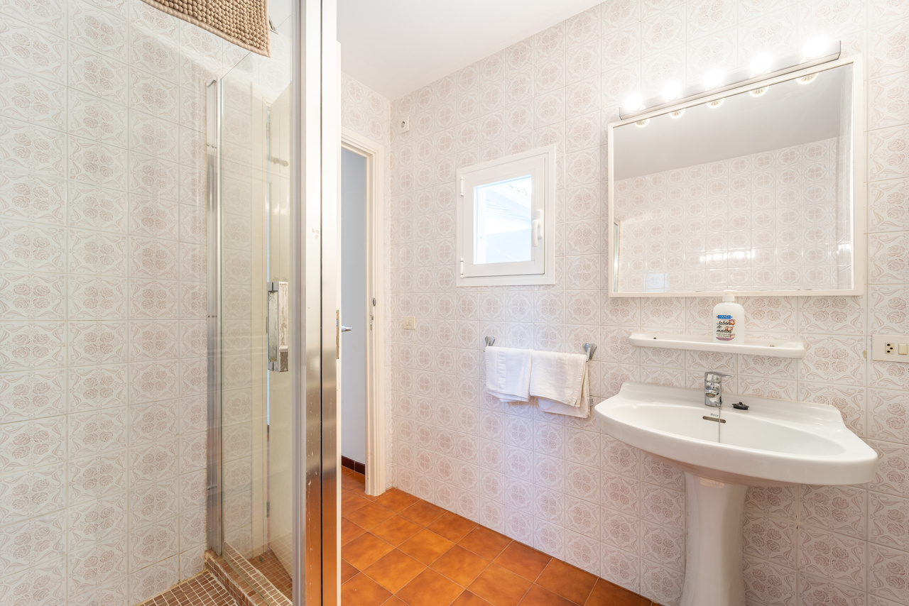 Cuarto de baño con ducha con mampara, lavabo con pie y espejo iluminado.