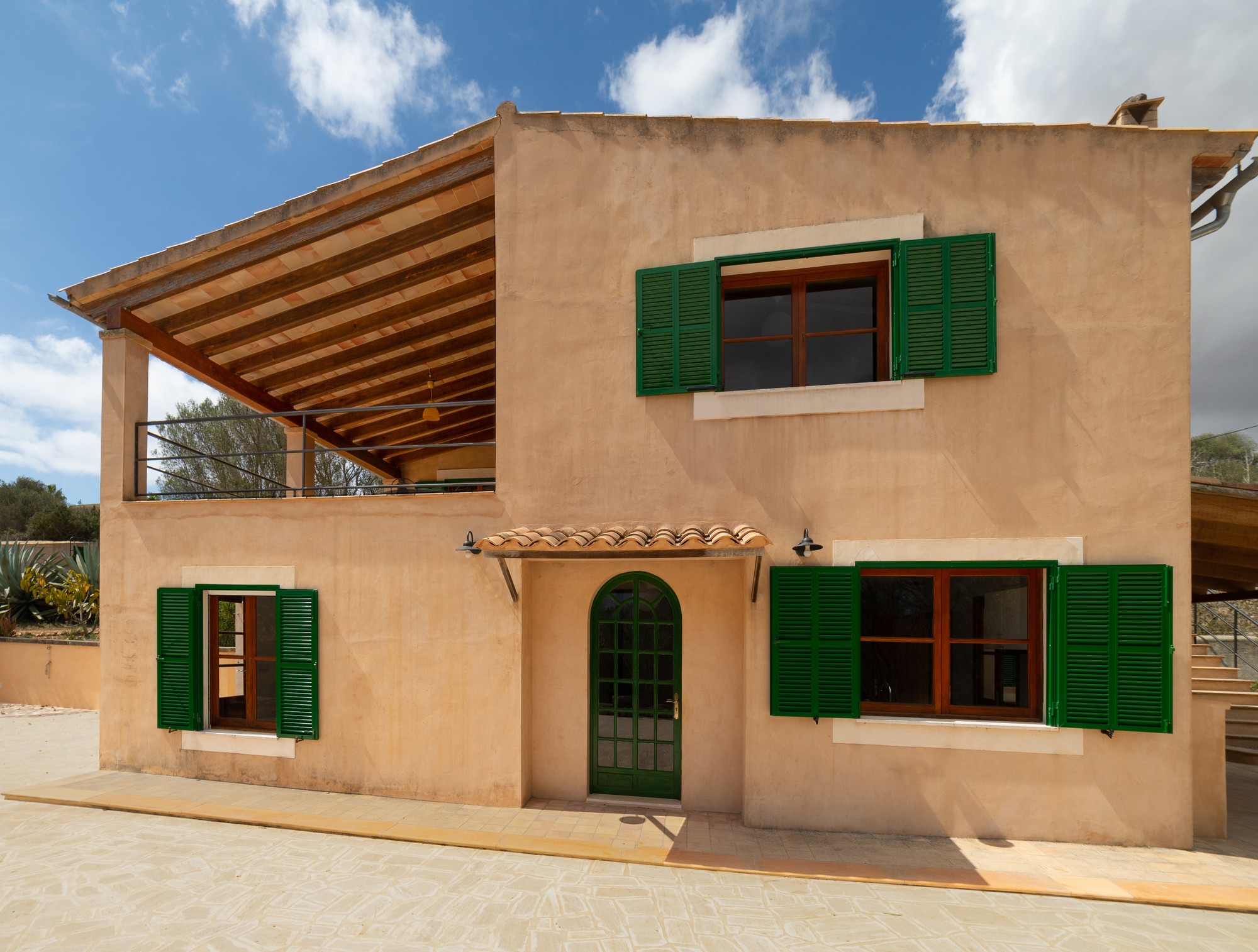 Fachada de una casa de campo mallorquina con porche de vigas y persianas verdes